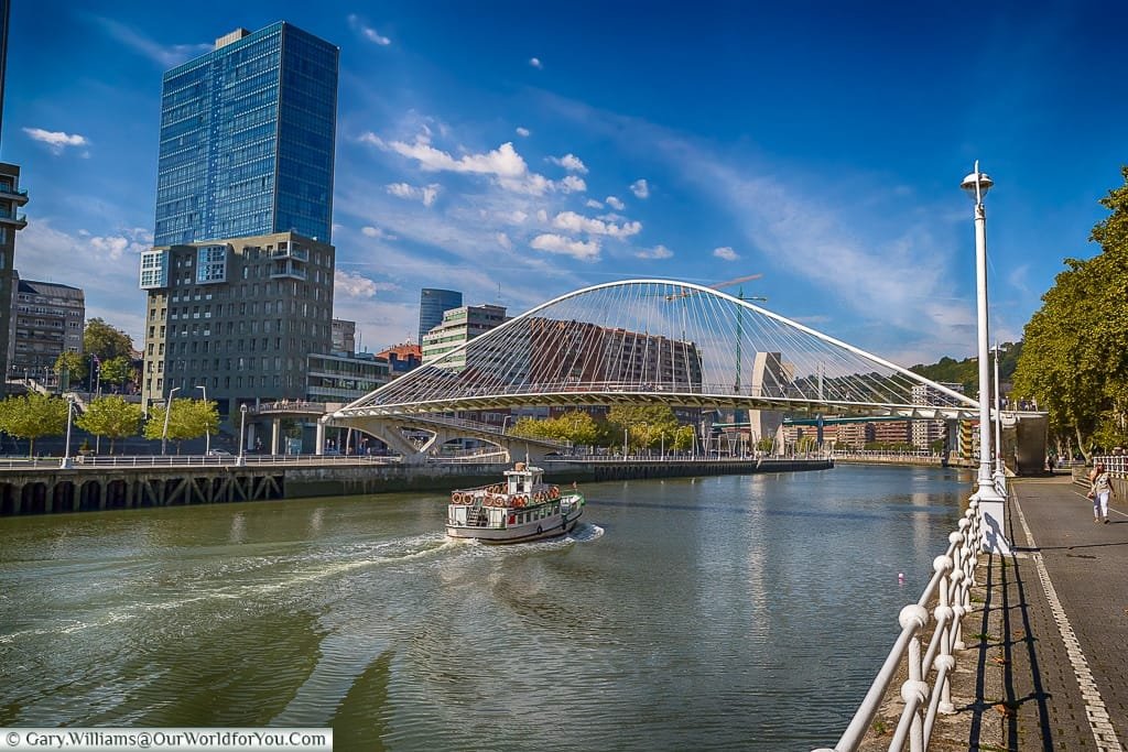 A boat motors under the Zubizuri or 'White Bridge', Bilbao, Spain