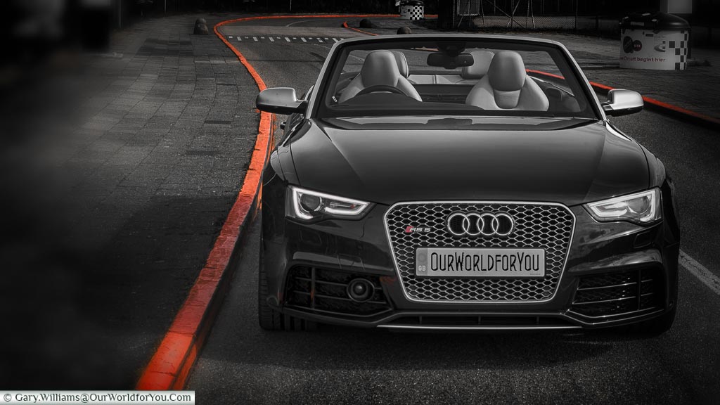 A stylised black, & white image of our Audi convertible parked at the edge of the road leading from the  Zandvoort Racing circuit, with the curbstones contrasted in Dutch Orange