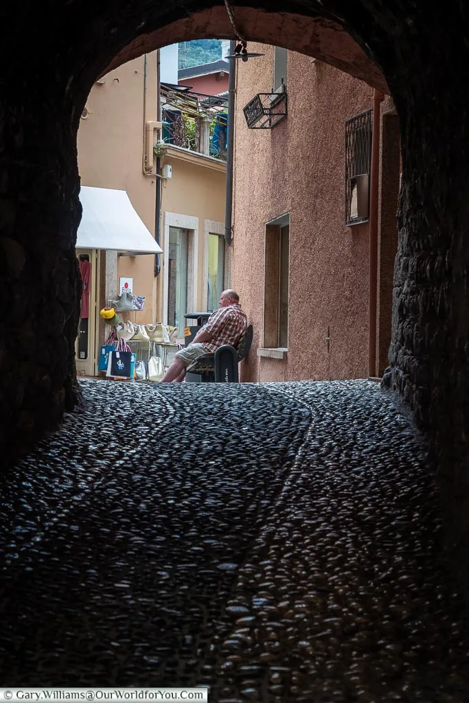 A look through a darkened archway to a man resting on a bench.