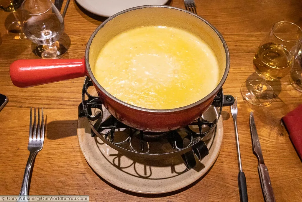 A bubbling pot of cheese fondue served in a cast-iron saucepan over a low heat.