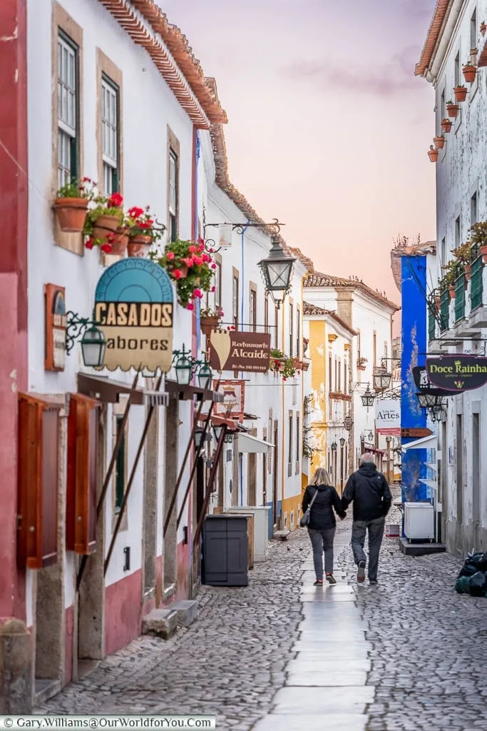 A couple walking along the main thoroughfare of old Óbidos town dusk.