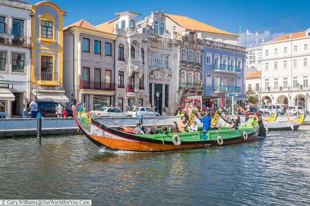 A colourful tourist Moliceiros boat in front of the beautiful classical architecture on the edge of the canal in Aveiro, Portugal