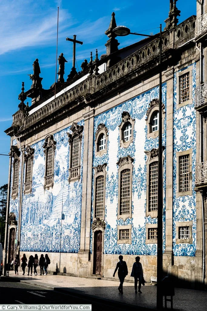 The silhouettes of people walking past blue-tiled baroque Igreja do Carmo in Porto, Portugal