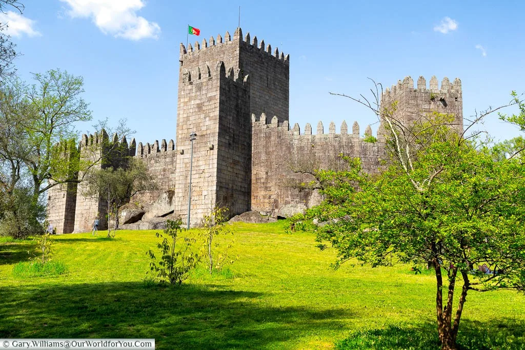 A Portuguese flag flying from a tower of Guimarães Castle behind its defensive walls set on a grassy bank