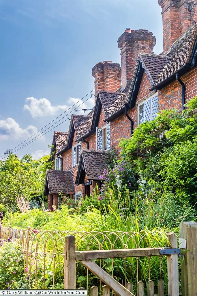 A row of red-brick terrace cottages, with beautiful old English styled country front gardens