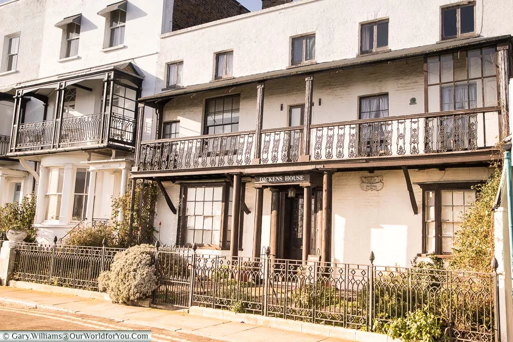 The entrance to Dickens house the traditional sea front home of a Georgian style predominately white with black trim features and black railings in front of a small garden.