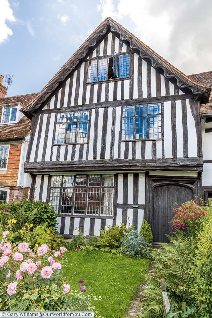 A black and white half-timbered Tudor period home with a cottage garden to the front. One of the older houses in Cranbrook