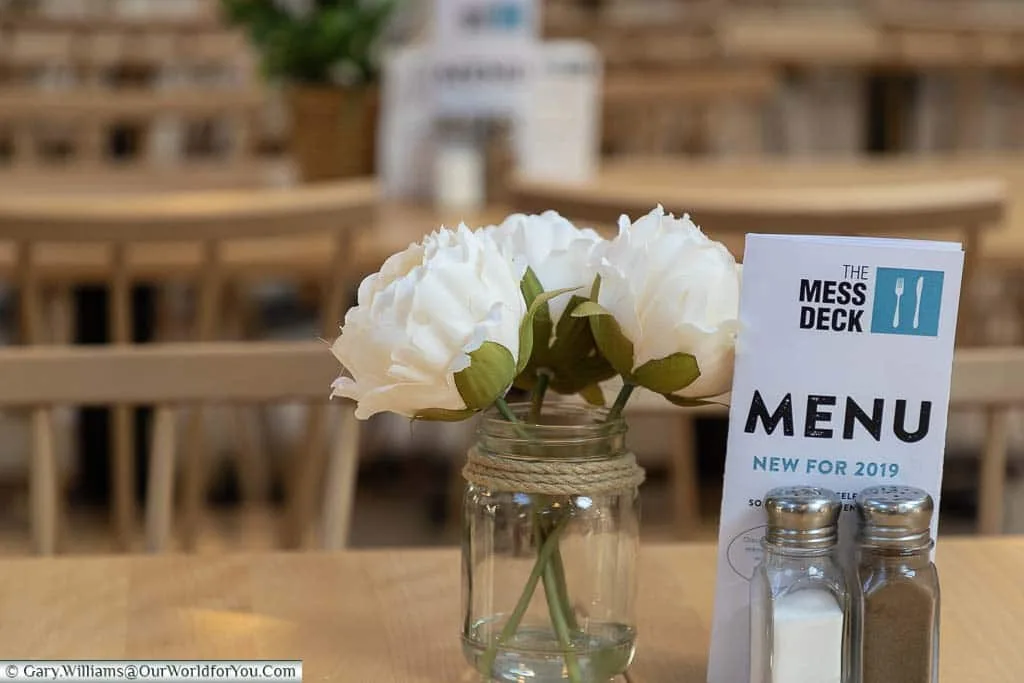 Three white flowers in a glass jar set on a table in the Mess Deck restaurant area of Historic Dockyard Chatham