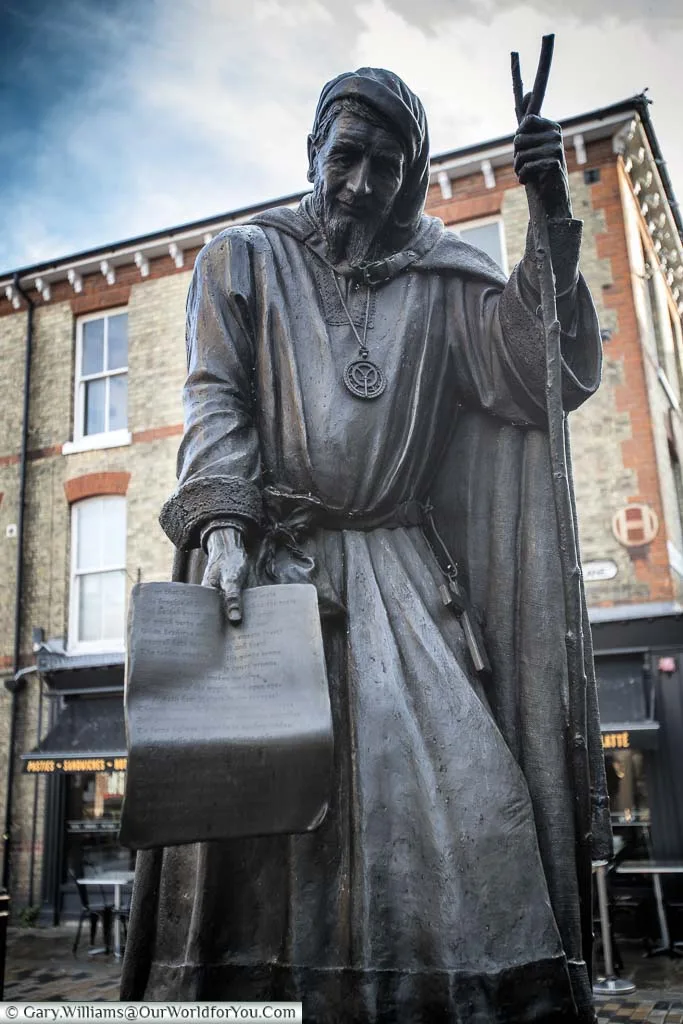 A statue to Geoffrey Chaucer, dressed as a pilgrim, sharing his Canterbury Tales, in the High Street of Canterbury, Kent.