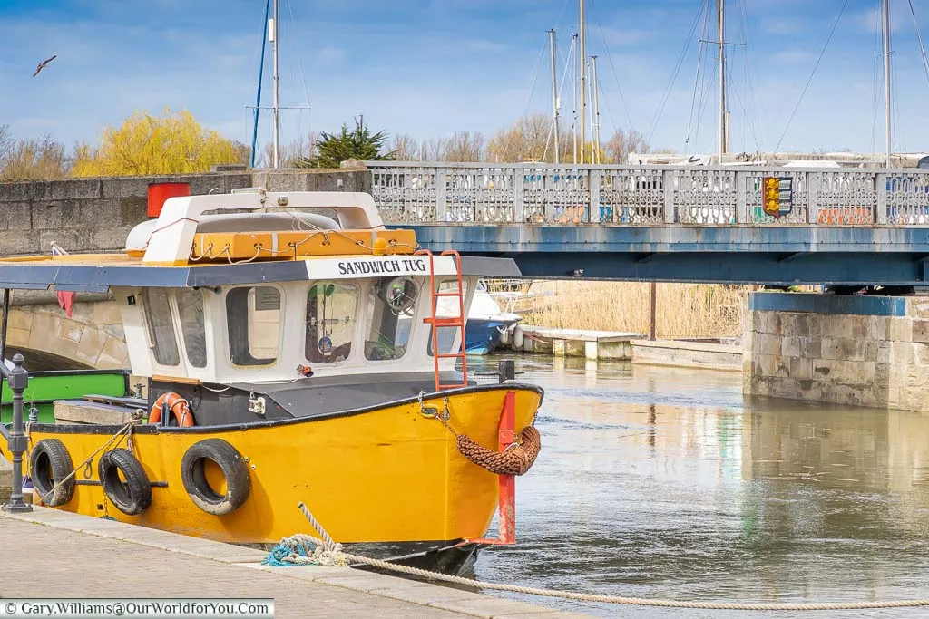 A yellow boat named The Sandwich Tug on the River Stour in Sandwich.