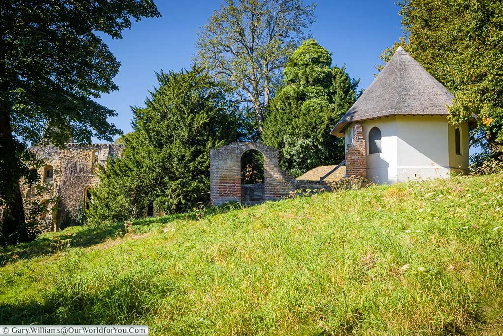 A view of a meadow in front of the small octagonal thatched Victorian Dairy building.