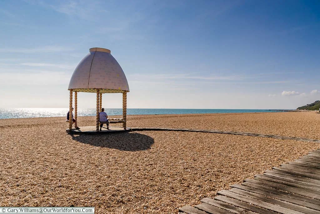 A small pavilion in the shape of a jelly mould reached by a wooden walkway on the shingle Folkestone beach