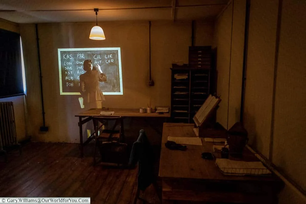 Inside a hut at Bletchley Park, with a holographic wartime codebreaker working on a code on a blackboard.