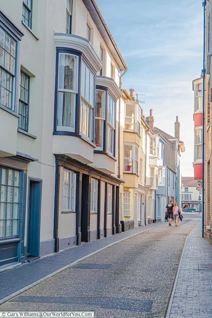 A couple walking along the narrow Jetty street, lined by colourful terraced period homes, towards Cromer town centre.