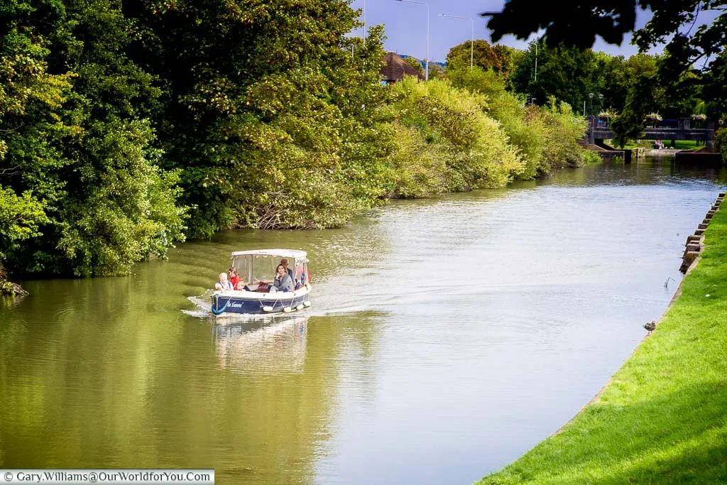 A small covered motorboat heading along the Royal Military Canal in Hythe, Kent