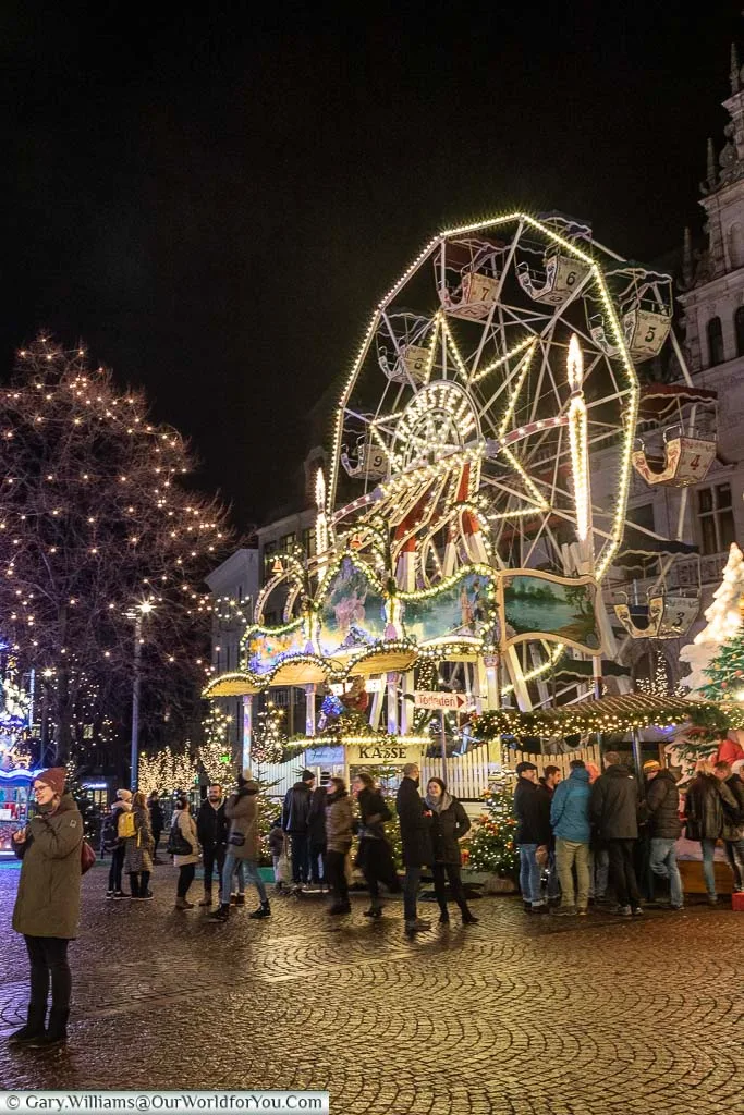 A group of people in front of a small, brightly lit, children's Ferris wheel.