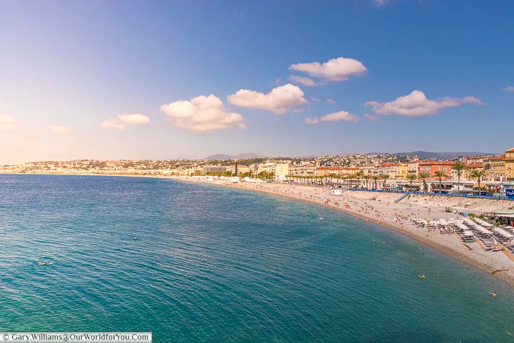 Beautiful blue waters leading up to the beach of Nice in southern France with holiday makers making the last of the autumn sunshine.