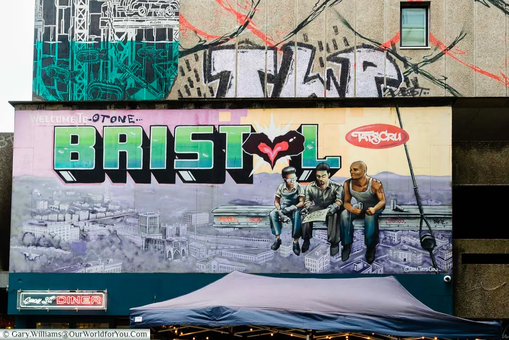 A mural above the Quay Street Diner depicting the members of the Tats Cru on an iron girder against a backdrop of Bristol