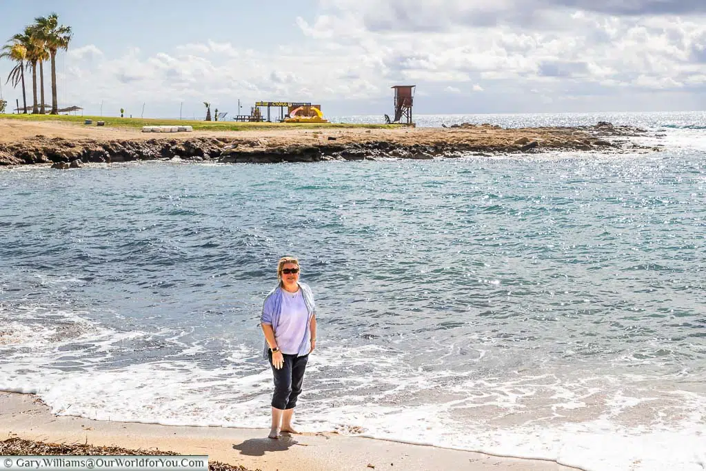 Janis standing with her feet in the Mediterranean sea in the bay next to the Olympic Lagoon Resort Paphos, Cyprus
