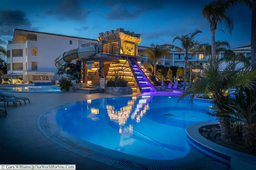 The illuminated Myayn Temple water slide at the Olympic Lagoon Resort Paphos at dusk.