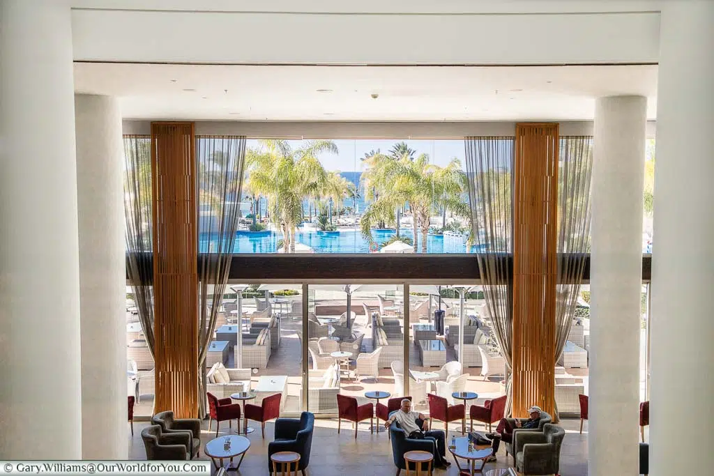 The view from the lobby of the Olympic Lagoon Resort Paphos, to the lounge below, looking onto the outside seating, pool and the Mediterranean sea beyond.