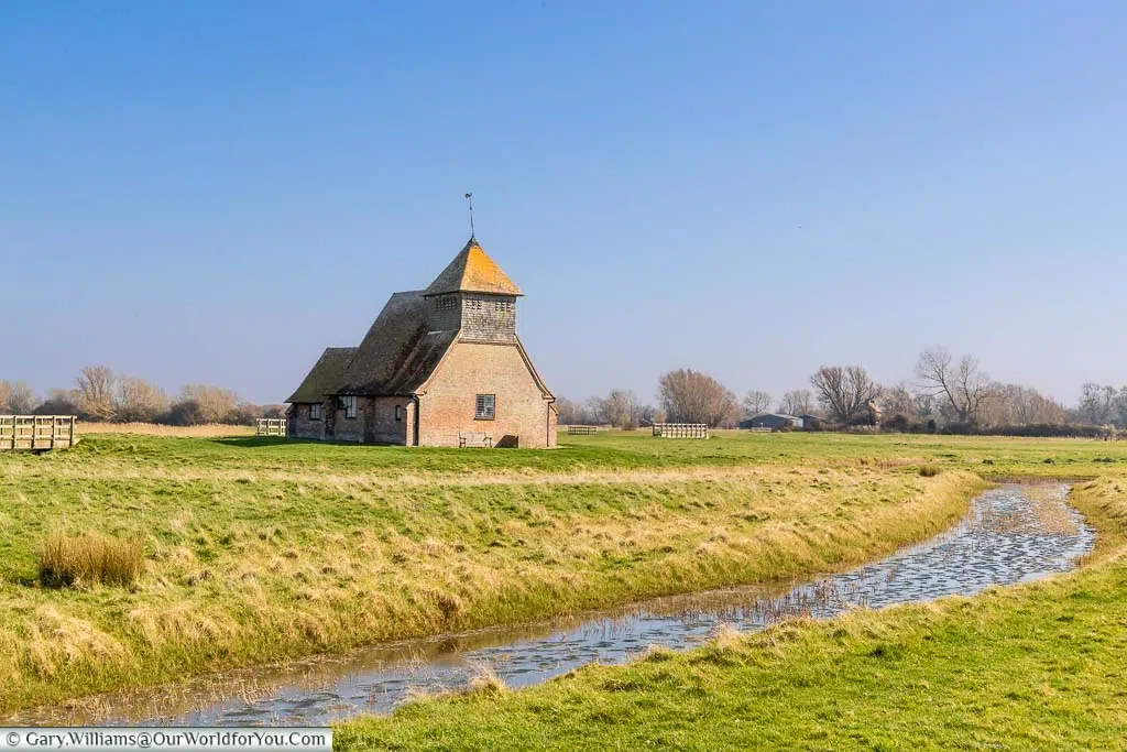 An open water channel leading past St Thomas Becket Church at Fairfield on the Romney Marshes in Kent