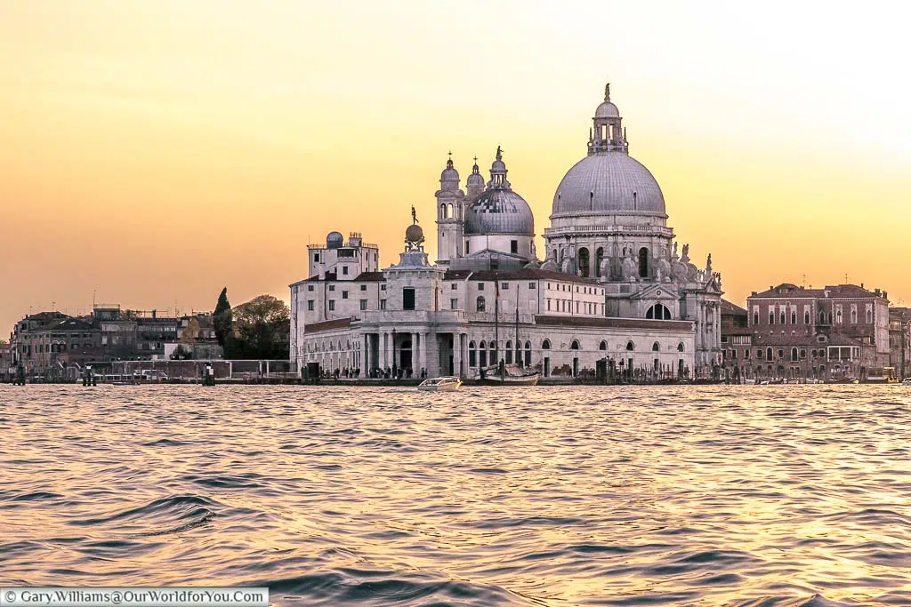 A shot of Santa Maria della Salute at dusk under an orange sky taken from a boat on the lagoon