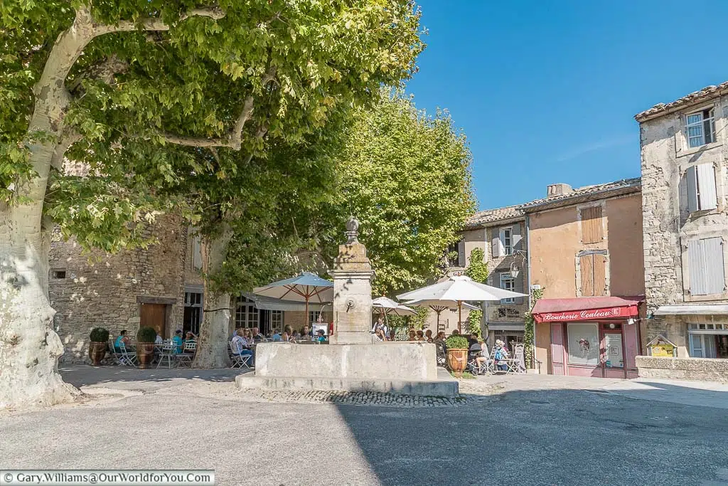 A fountain in a square with dinners enjoying lunch under the shade of trees.