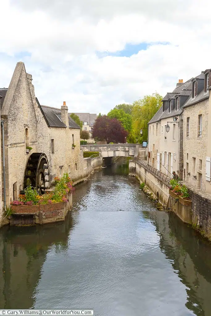 A view of a waterwheel, surrounded by flowers, in the River Aure in Bayeux.