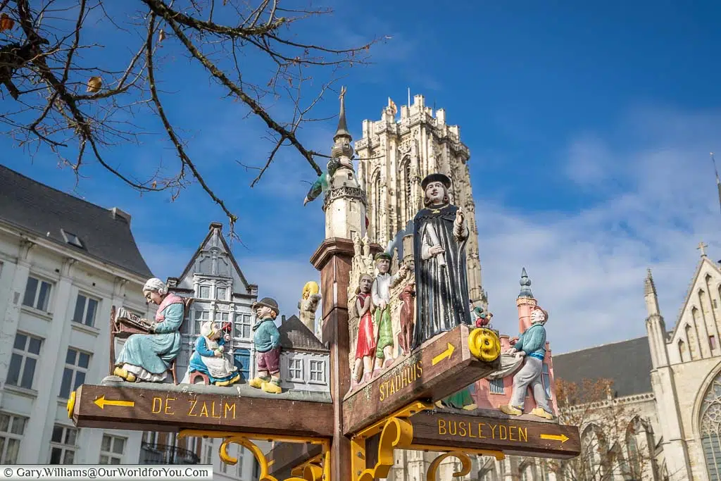An ornate wooden sign with figures from Mechelen's history with St Rumbold's Tower in the background.