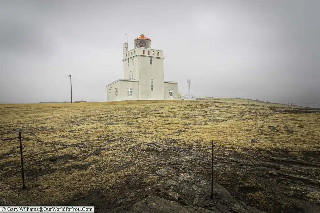 The cream coloured brick-built lighthouse topped by a red coloured lamp enclosure on top set high on a rocky outcrop