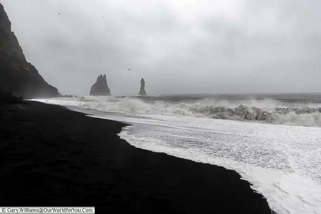Waves breaking on the Reynisfjara Beach on a stormy day with Basalt Rock pillars in the background