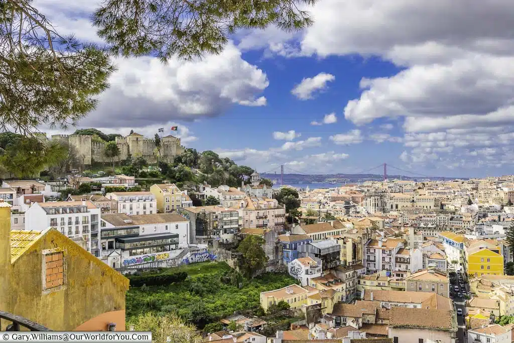 The view from Miradouro da graça over the rooftops of Lisbon, Portugal. In the near distance you can see the castle on the hillside, and in the distance the April 4th Bridge over the River Tagus