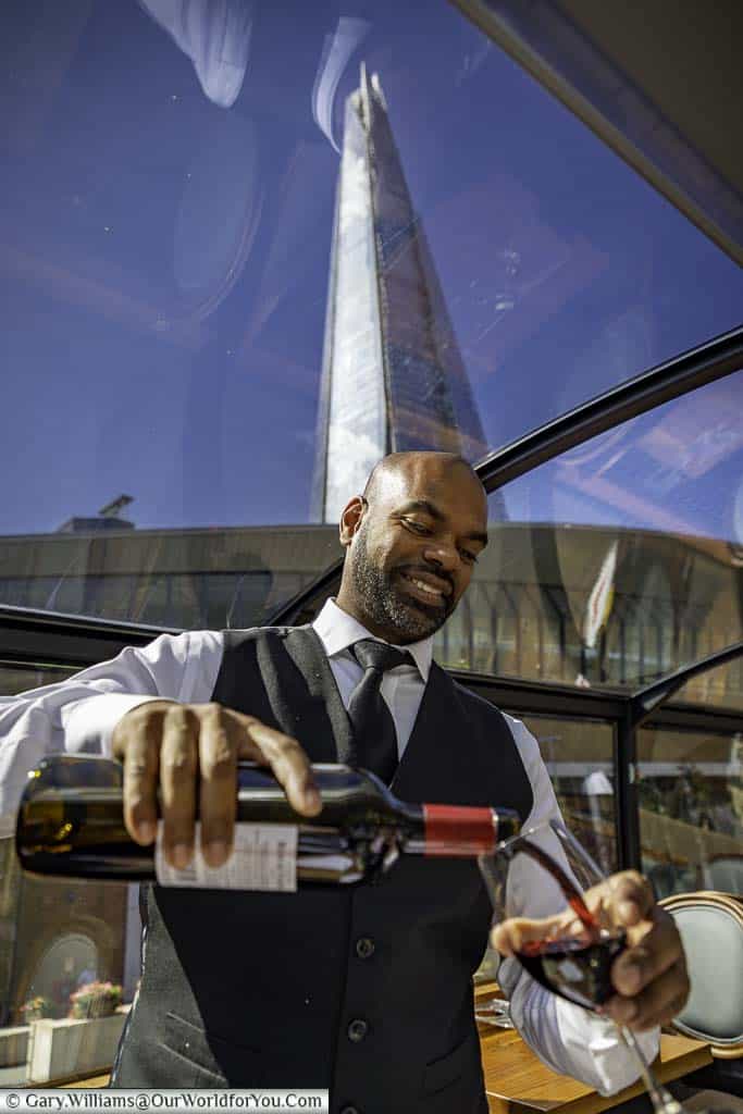 Jerome, our waiter, pouring us a glass of red wine with The Shard in the background visible through the panoramic roof.