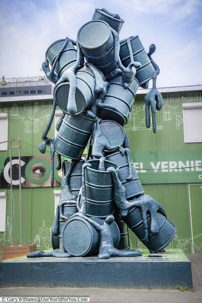 An eight-metre tall sculpture named 'Cascade', of eighteen stacked oil drums, which appear to descend from the sky like a waterfall. From the life-size drums drips a syrupy mass in which one can make out the shapes of a score of human figures.