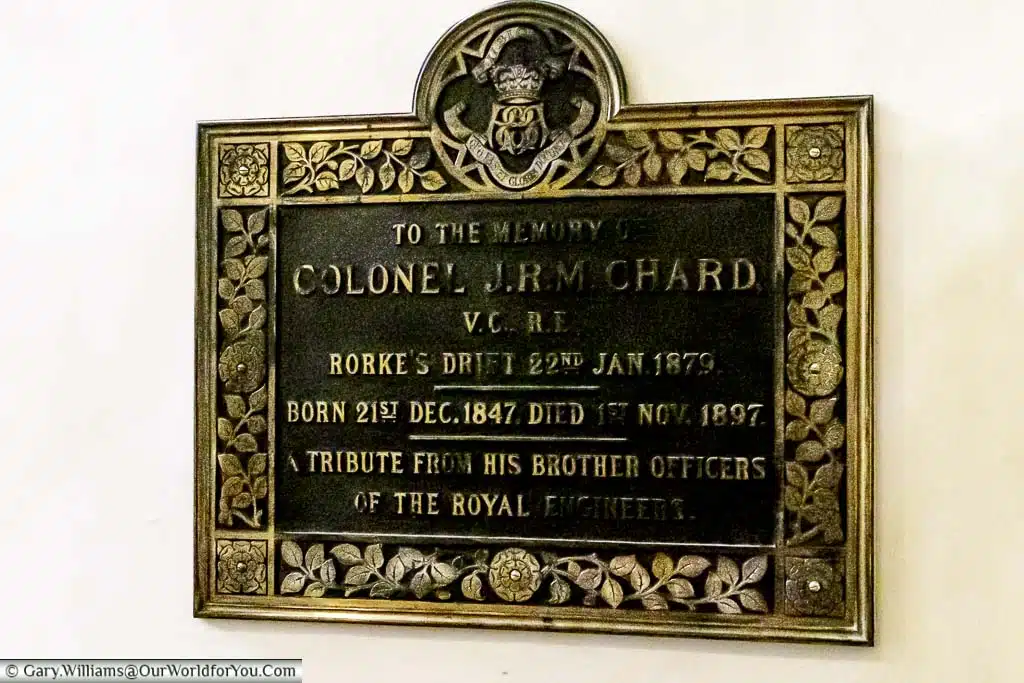 A tired-looking plaque of raised brass against a dark iron to Colonel J.R.M. Chard VC in rochester cathedral