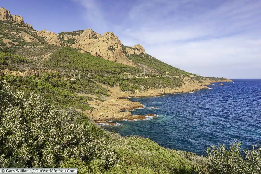 A view of the rugged red rocks and the deep blue waters of the Cote d'Azur. Hugging the coastline is the road known as the Corniche d'Or.