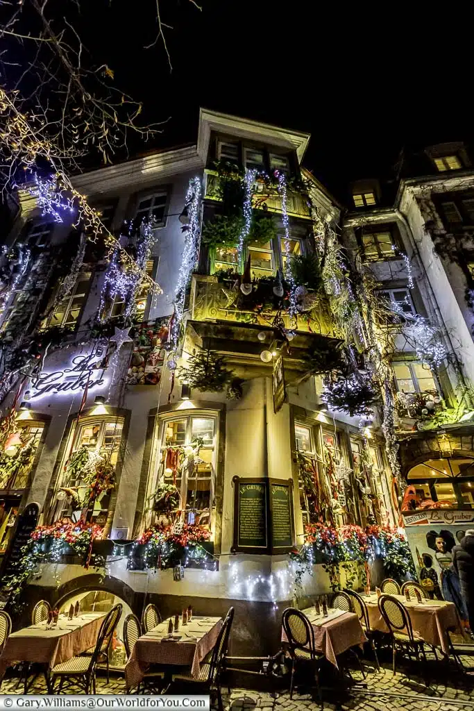 The restaurant Le Gruber with tables and chairs outside at night decorated for Christmas with fairy lights, baubles and glittery bunting.