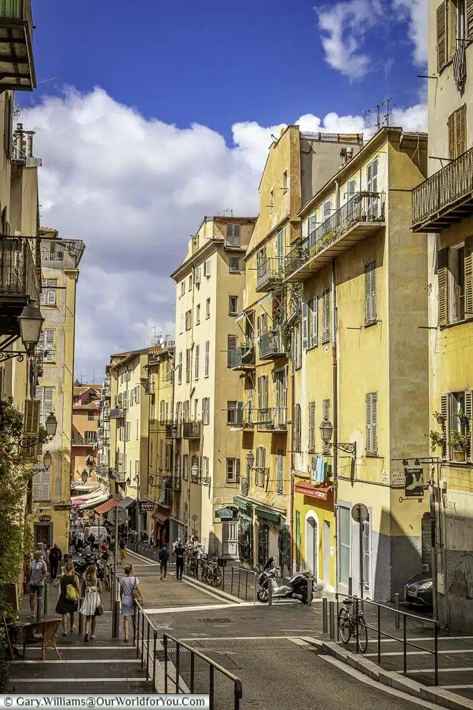 A narrow street through the old town of Nice, lined on either side by brightly coloured buildings