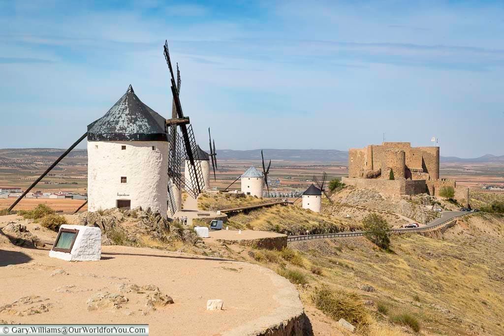 The windmills of consuegra to the castle in the distance against the backdrop ofthe flat landscape of la mancha