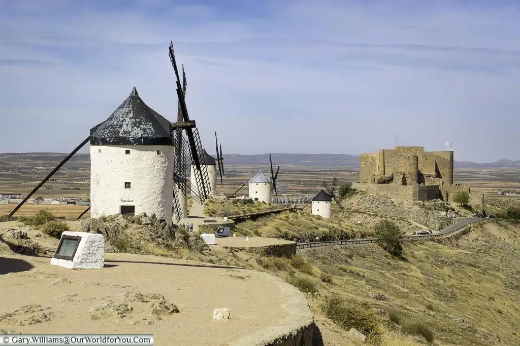 The windmills of consuegra to the castle in the distance against the backdrop ofthe flat landscape of la mancha