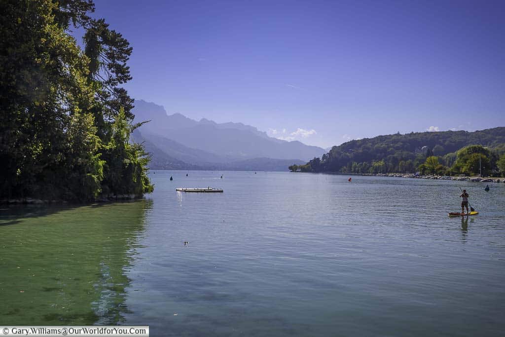 a lone paddleboarder on lake annecy in france under clear blue skies