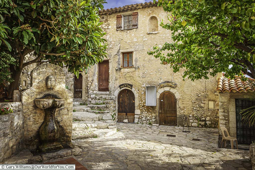 A water fountain in a quiet courtyard of the sleepy hillside town of èze, surrounded by rustic, golden stone buildings.