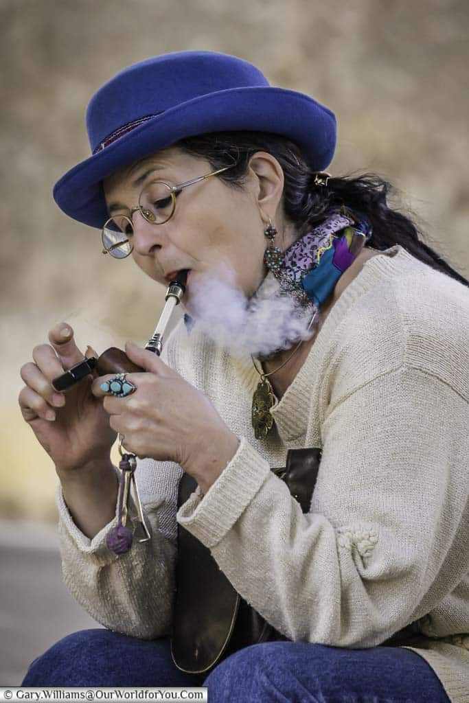 An elegant dressed, mature seated woman wearing a blue felt hat, smoking a pipe in st paul de vence in the south of france