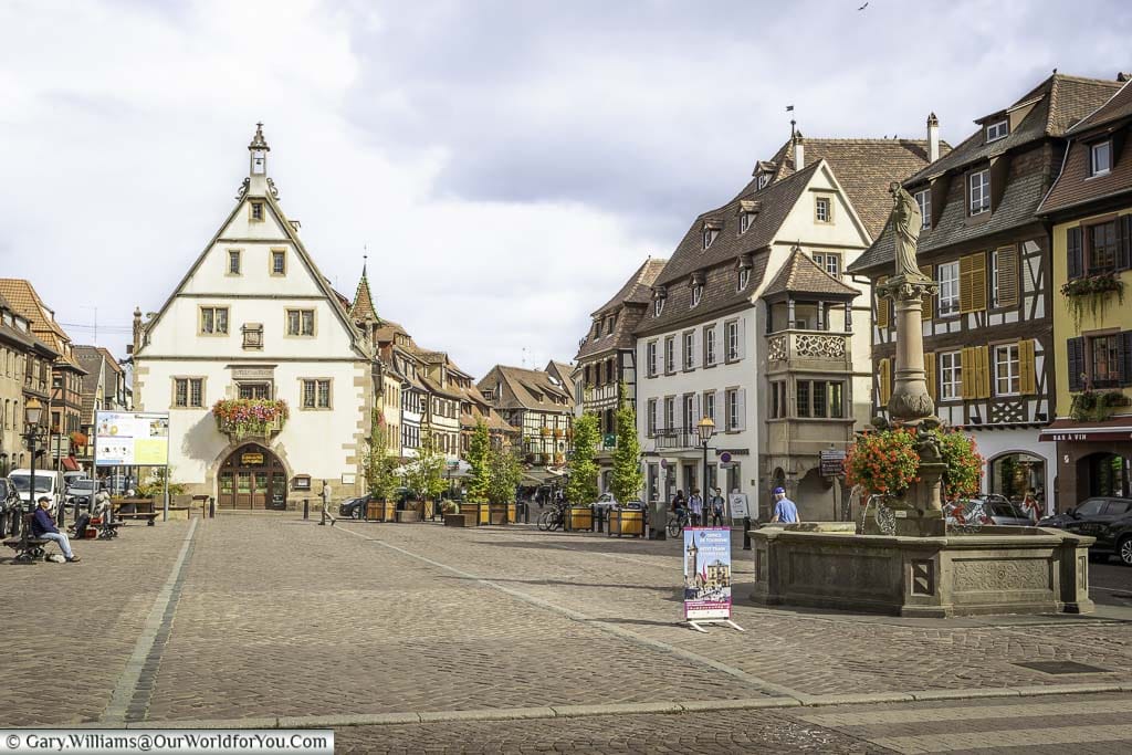 A stone fountain in the town square in Obernai, in the Alsace region of France, lined on all sides by historic half-timbered buildings of the region