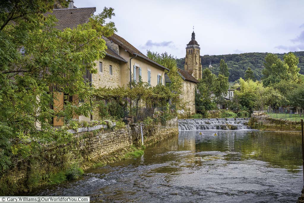 an idylic rural french scene as the cuisance river flows over some rocks as it makes its way past stone built rustic homes in arbois in the jura region of france