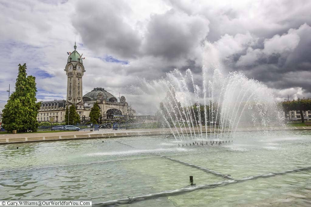 A fountain in le jardin du champ de juillet with the tower of limogues railway station