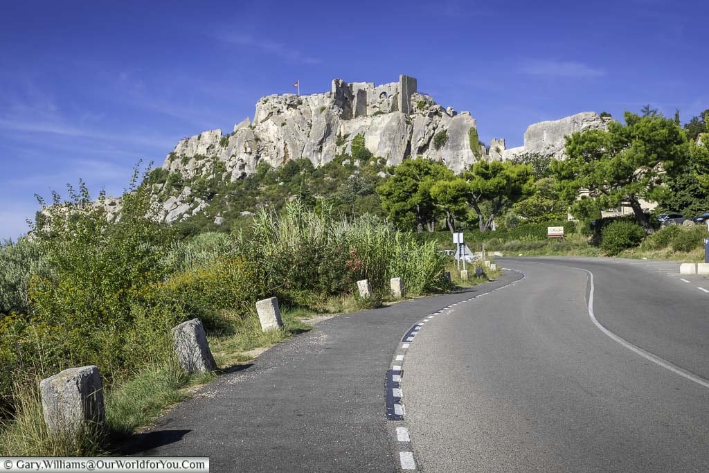The roadside curves up towards the hillside village of Les Baux-de-Provence. The remains of the ruins of Château des Baux sit high on the rock face.