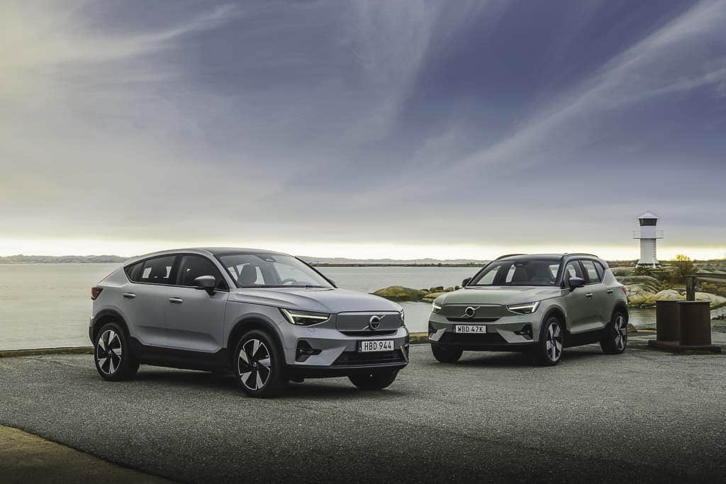 A stock photo of two Volvo XC40's at the water's edge with a small lighthouse in the background