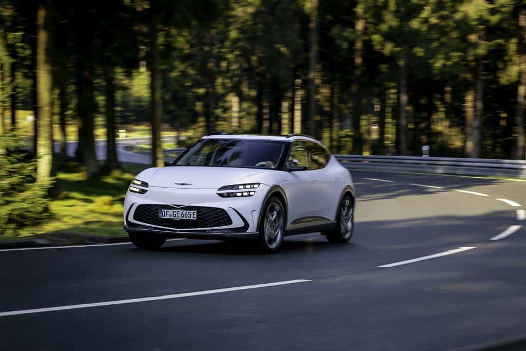 A stock photo of a Genesis GV60 Driving around a corner on a forest road